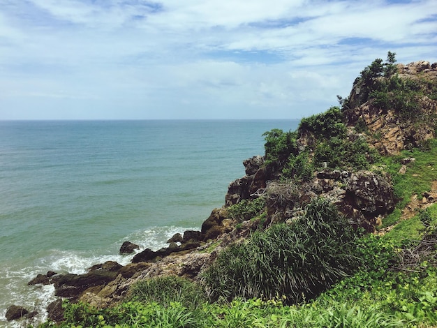 Vista panorâmica do mar por formação rochosa contra o céu nublado