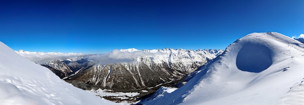 Vista panorâmica dos picos das montanhas nevadas no céu azul das nuvens do Cáucaso