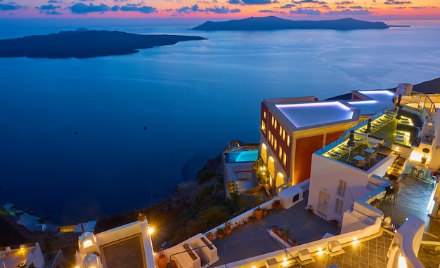 Vista panorámica con edificios iluminados en la costa de la isla de Santorini y el mar Egeo al anochecer, Fira, Grecia. Paisaje