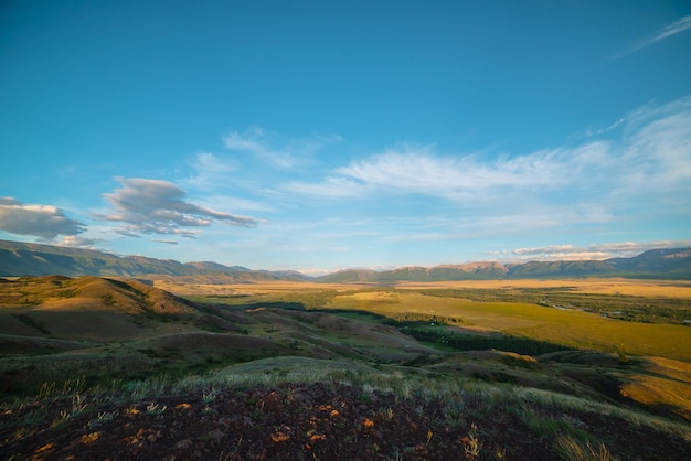 Vista panorámica escénica desde la colina cubierta de hierba hasta el bosque iluminado por el sol y la estepa dorada contra la alta cordillera bajo la luz del sol dorada Colorido paisaje soleado con estepa y grandes montañas bajo el sol dorado