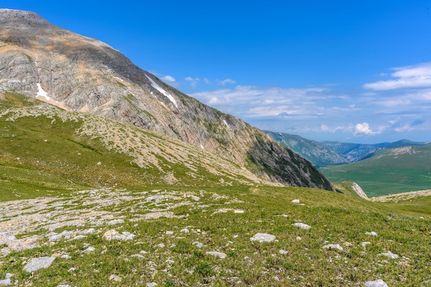 Vista panorámica escénica de idílicas colinas paisaje con prados en flor y picos montañosos alpinos cubiertos de nieve Un hermoso día soleado con cielo azul y nubes en primavera