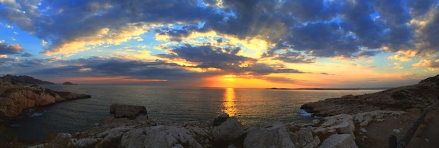 Vista panorámica de la formación rocosa y el mar contra el cielo nublado durante la puesta de sol