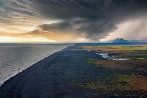 Vista panorámica de la hermosa playa de arena negra contra el cielo nublado durante la puesta de sol