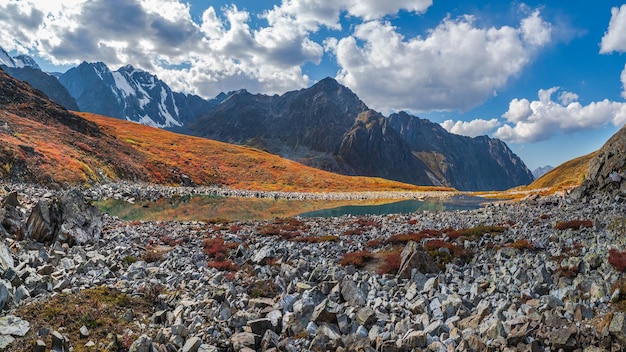 Vista panorámica del lago de montaña de otoño con nubes blancas de reflexión Un lago de montaña azul claro y piedras de otoño brillantes flotando en el agua