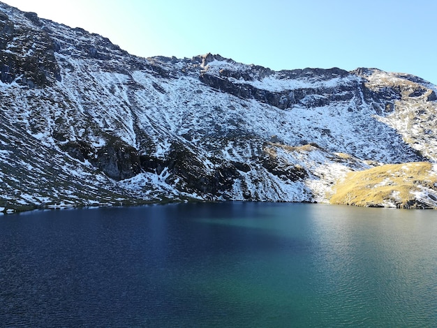 Foto vista panorámica del lago por las montañas cubiertas de nieve contra un cielo azul claro