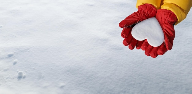 Vista panorámica de la mano en guante rojo tiene corazón de nieve