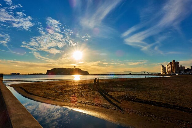 Vista panorámica del mar y silueta de personas contra el cielo durante la puesta de sol