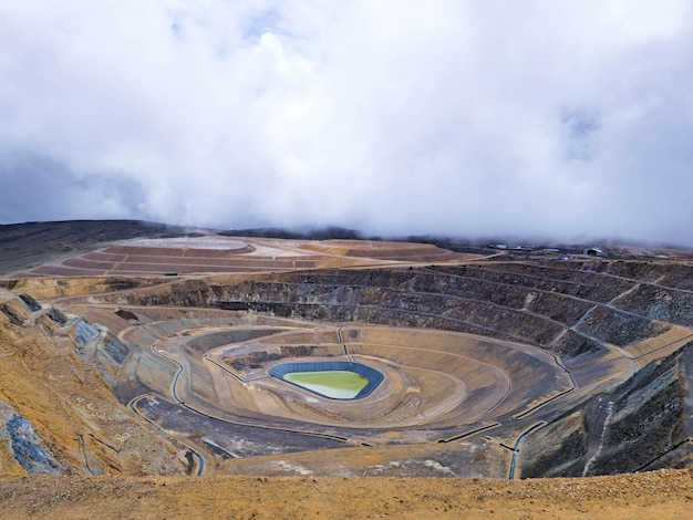 Vista panorámica de una mina a cielo abierto con una laguna en el fondo y clima lluvioso