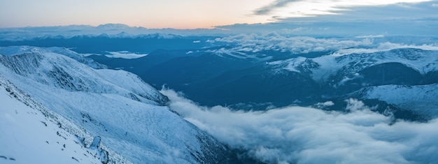 Vista panorámica de las montañas nevadas temprano en la mañana, niebla y nubes en el valle