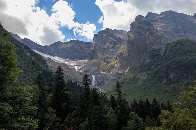 Vista panorâmica na cena de montanhas e cachoeira distante no Parque Nacional de Dombay, Cáucaso, Rússia. Paisagem de verão, clima ensolarado e dia ensolarado