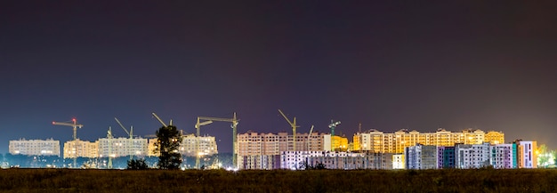 Vista panorámica nocturna de muchas grúas de construcción en el sitio de construcción de la nueva zona residencial moderna