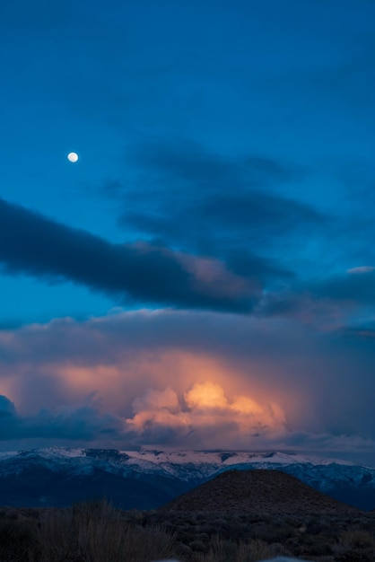 Foto vista panorámica del paisaje al amanecer con luz dorada en las nubes y luna llena en el cielo azul