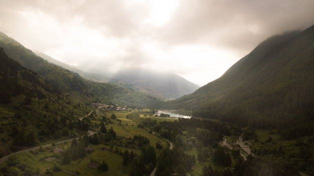 Vista panorámica del paisaje de montaña rural verde con árboles, carreteras y lago. Paisaje de campo verde con silueta de montaña contra el cielo nublado. Camino a la montaña a lo largo del lago y el campo verde.