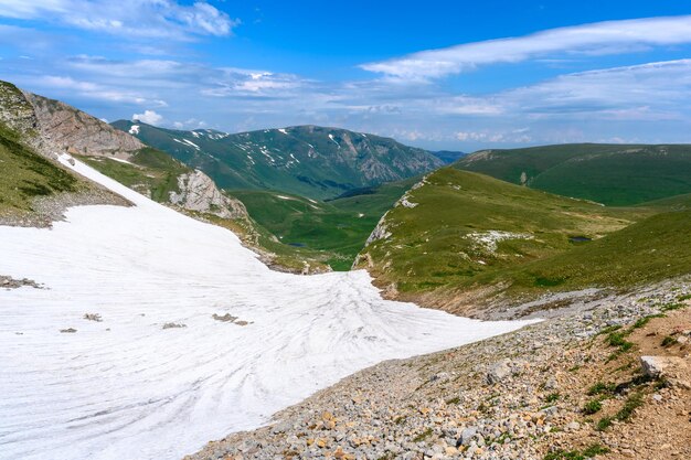 Vista panorâmica panorâmica de idílicas colinas paisagem com prados em flor e picos alpinos cobertos de neve no fundo em um belo dia ensolarado