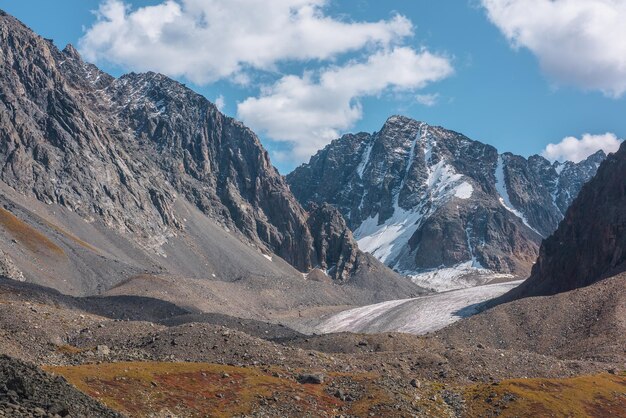 Vista panorámica de las rocas iluminadas por el sol y la gran cima de la montaña nevada con glaciar en un día soleado de otoño Colores vivos del otoño en las altas montañas Paisaje abigarrado con rocas afiladas y el pico de la montaña nevada bajo el sol brillante