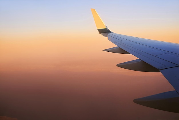 Vista para a asa do avião no céu durante o pôr do sol