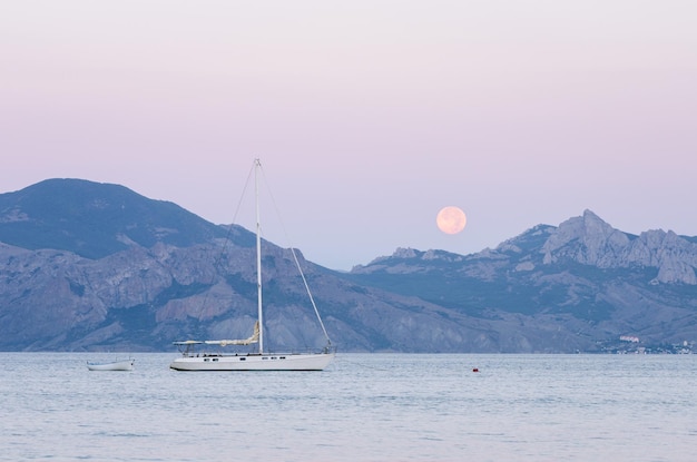 Vista para o mar com iate à vela. Lua cheia no cume. Paisagem de verão ao entardecer perto da cidade turística