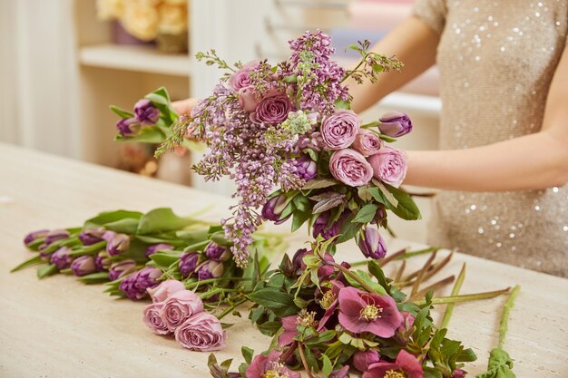 Foto vista parcial de florista fazendo buquê de tulipas, peônias e lilas no local de trabalho