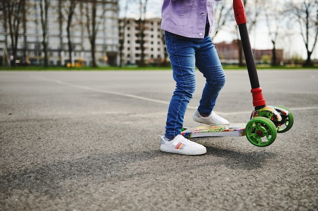 Vista parcial de uma menina andando de scooter ao ar livre contra edifícios desfocados da cidade