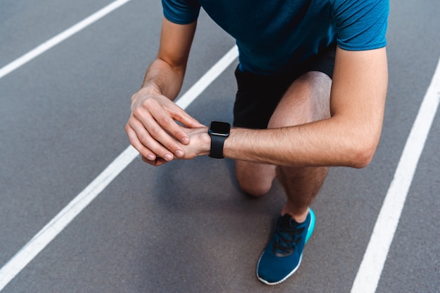 Vista parcial del joven deportista atlético mirando smartwatch en la pista de atletismo