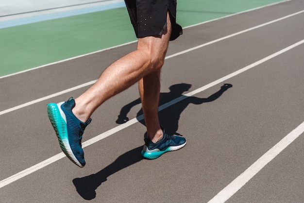 Vista parcial del joven deportista atlético en zapatillas para correr en la pista de atletismo