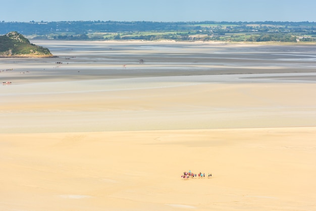 Vista desde las paredes del Mont Saint Michel en la bahía durante la marea baja con grupos de turistas caminando. Francia