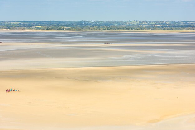 Vista desde las paredes del Mont Saint Michel en la bahía durante la marea baja con grupos de turistas caminando. Francia