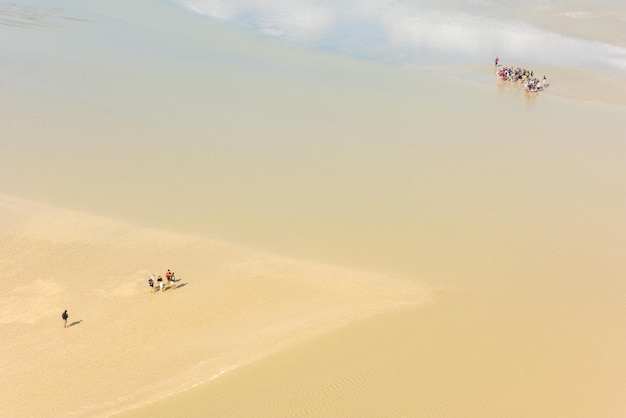 Vista desde las paredes del Mont Saint Michel en la bahía durante la marea baja con grupos de turistas caminando Francia