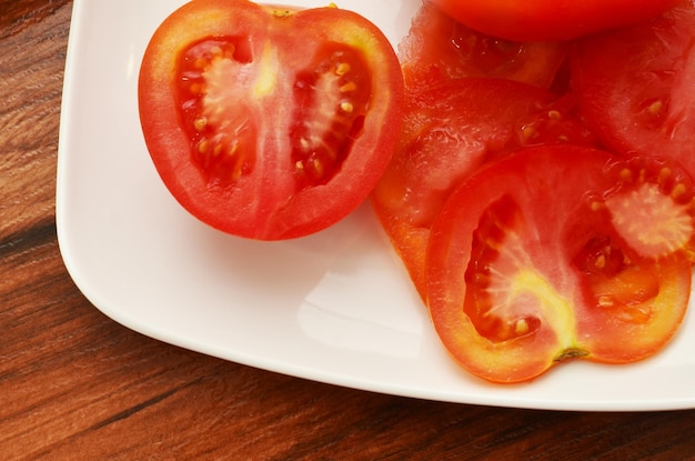 Vista de parte de un plato blanco con rodajas y la mitad de tomate rojo fresco con vista lateral.