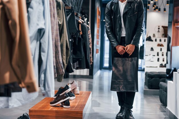 Vista de partículas Chico joven en una tienda moderna con ropa nueva Ropa elegante y cara para hombres