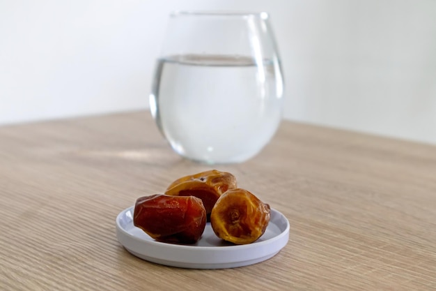 Foto vista de un pequeño plato de dátiles en una mesa de madera con un vaso de agua en el fondo