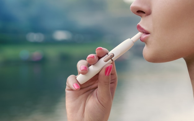 Vista de perfil de cara de mujer adulta fumar cigarrillo electrónico al aire libre