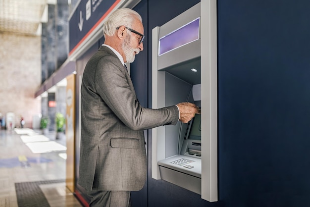 Foto vista de perfil de empresario senior en traje usando cajero automático para retiro de dinero en efectivo