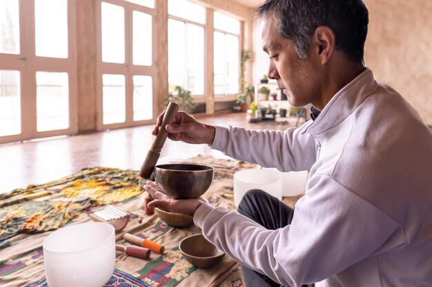 Foto vista de perfil de un hombre asiático de mediana edad jugando a un cuenco de bronce en una habitación iluminada