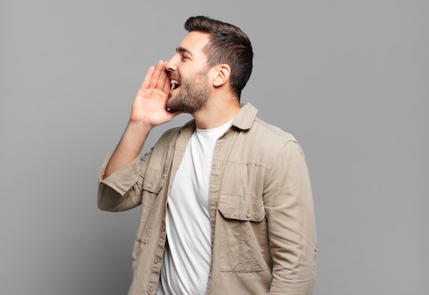 Vista de perfil de hombre rubio adulto guapo, luciendo feliz y emocionado, gritando y llamando para copiar espacio en el lateral