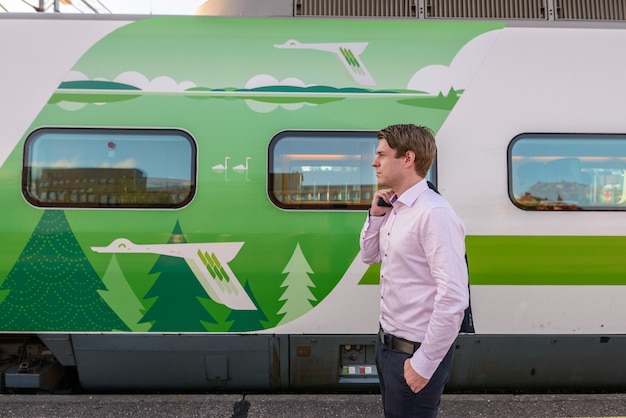 Foto vista de perfil del joven empresario guapo delante del tren en la estación de tren