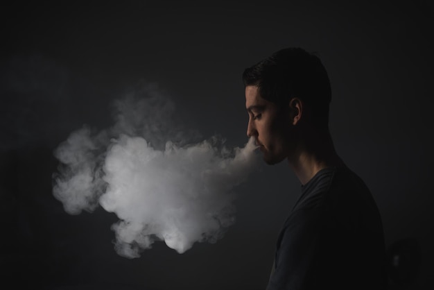 Vista de perfil de un joven fumando contra un fondo gris