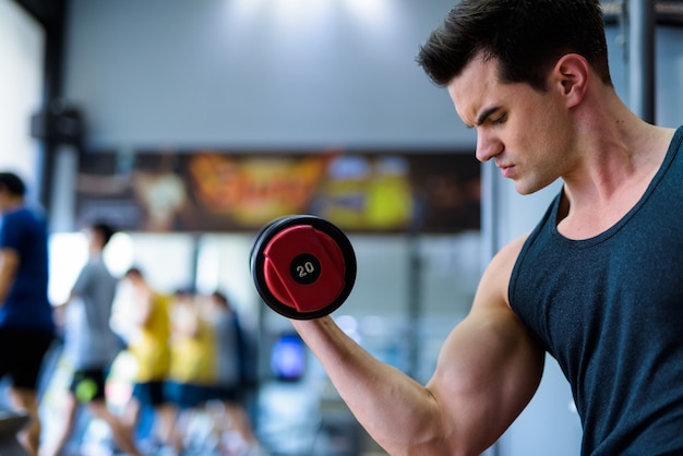 Vista de perfil de joven guapo haciendo ejercicio con pesas en el gimnasio