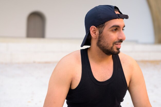 Vista de perfil de joven guapo indio barbudo con sombrero en las calles al aire libre