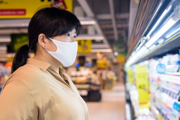 Vista de perfil de mujer asiática con sobrepeso con máscara de compras dentro de supermercado