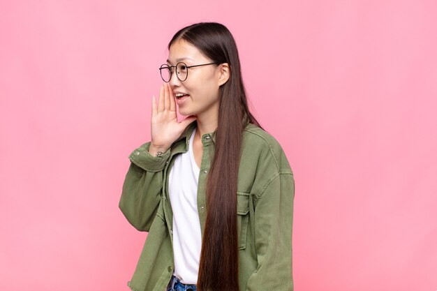 Vista de perfil de mujer joven asiática, luciendo feliz y emocionada, gritando y llamando para copiar espacio en el lateral