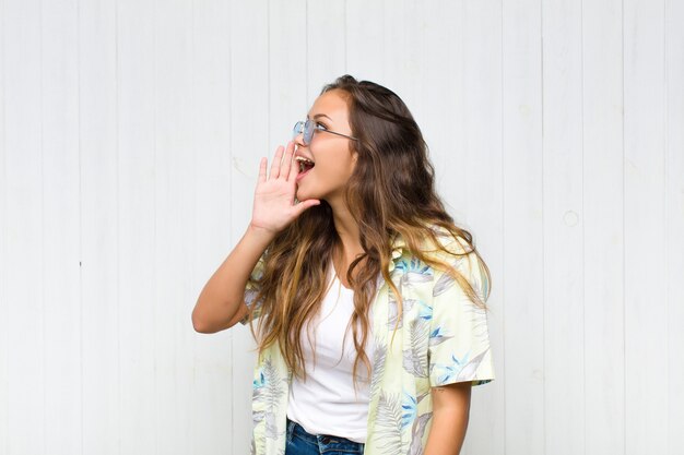 Vista de perfil de mujer joven y bonita, luciendo feliz y emocionada, gritando y llamando para copiar espacio en el lateral