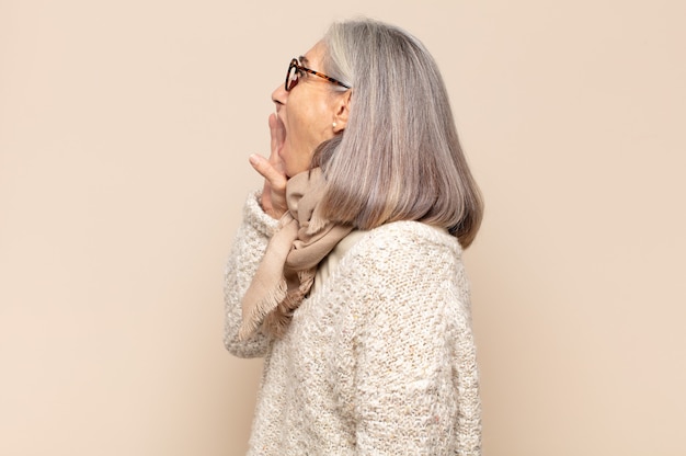 Vista de perfil de mujer de mediana edad, luciendo feliz y emocionada, gritando y llamando para copiar espacio en el lateral