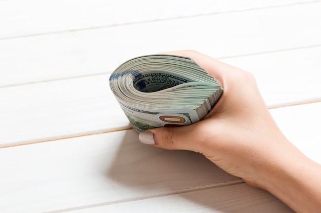 Vista en perspectiva de la mano femenina sosteniendo un paquete de dinero sobre fondo de madera. Cien dolares. Concepto de negocio. Concepto de caridad y consejos
