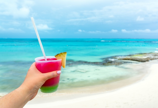 Vista en perspectiva personal de la mano femenina sosteniendo un vaso y bebiendo cócteles en el mar caribe