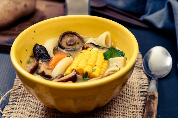Vista picada de uma deliciosa sopa caseira de frango, legumes e cogumelos com macarrão e milho. Conceito de comida natural e saudável