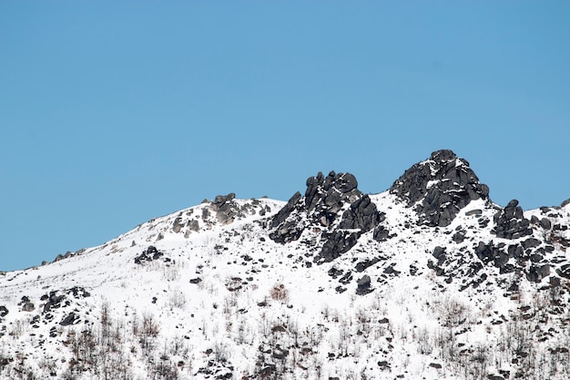 Vista de un pico de montaña rocosa cubierto de nieve en un día soleado.