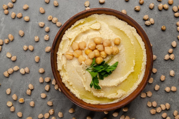 Vista plana en el hummus cubierto con hojas de cilantro verde sobre una mesa de piedra cubierta con garbanzos