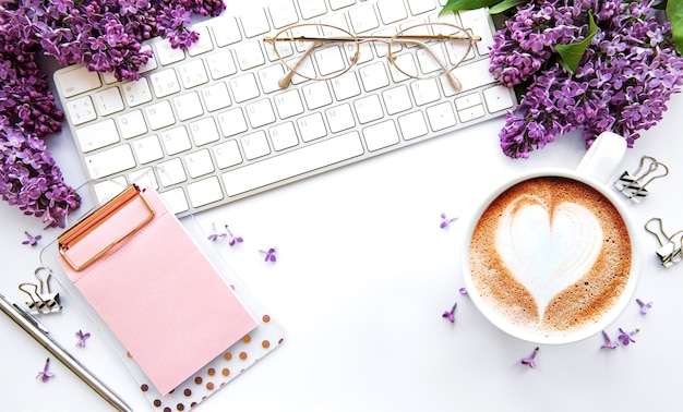 Vista plana leiga, mesa de escritório mesa superior. espaço de trabalho com teclado, flores lilás e material de escritório em fundo branco.