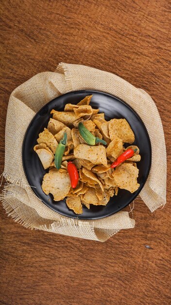 Vista plana de la merienda tradicional indonesia de Basreng hecha de albóndigas fritas con chile en polvo para sazonar servido en un plato negro
